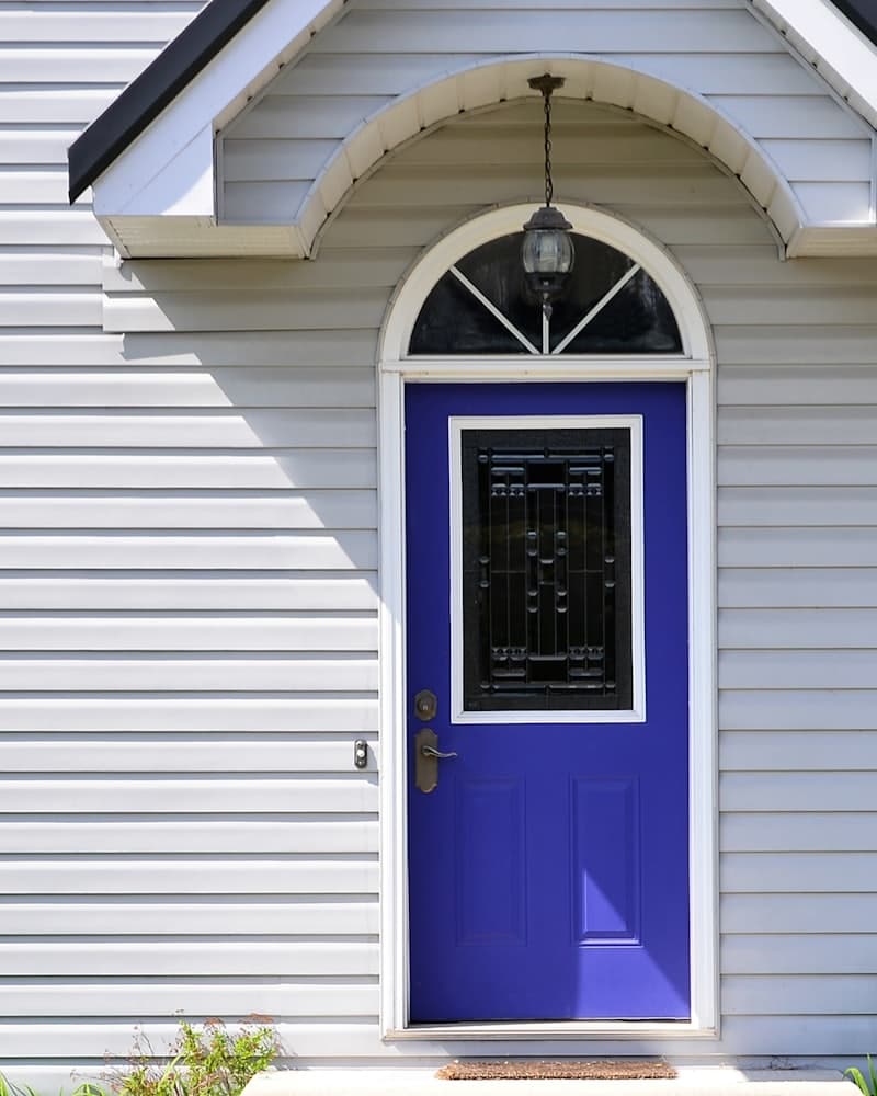A freshly painted violet front door on white siding